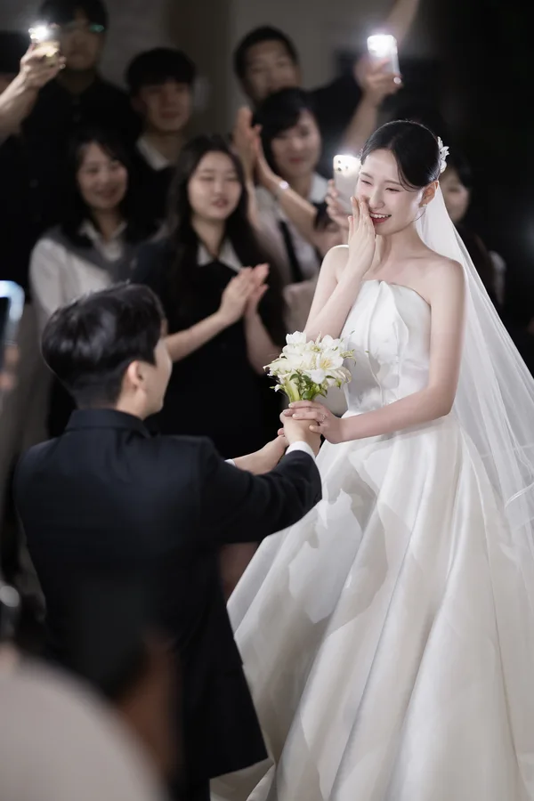 하객들의 환호와 조명 플래시 속 손을 맞잡은 신랑신부 신부가 감격한 표정을 짓는다