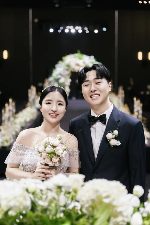 흰 꽃 너머로 얼굴을 맞대고 미소 짓는 신랑신부 상반신컷
